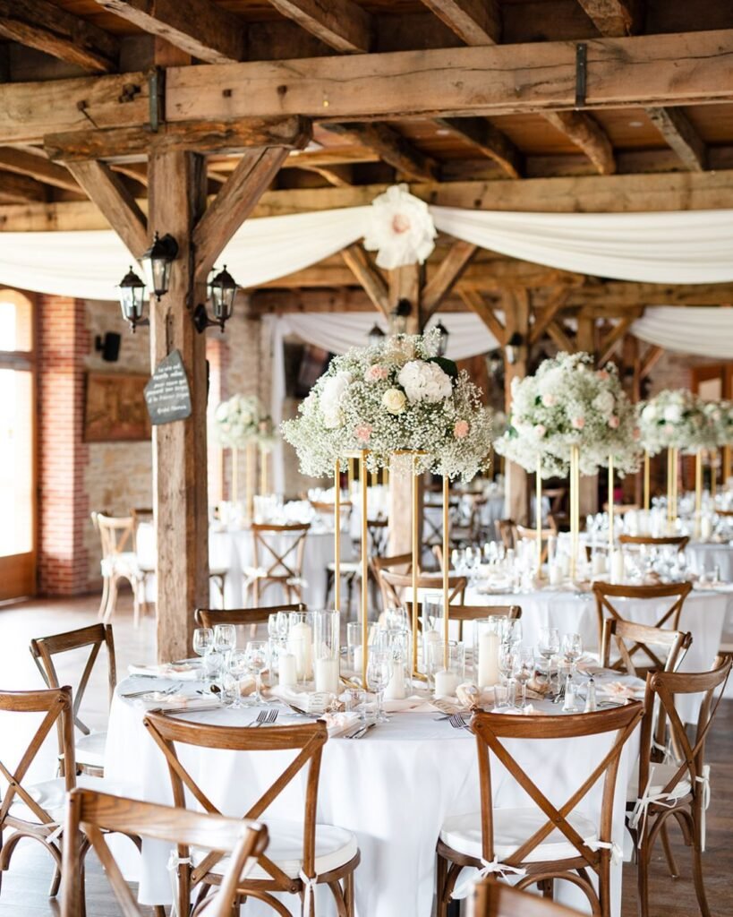 Charming rustic wedding reception decor with elegant floral centerpieces and wooden beams at Domaine d'Essendiéras.