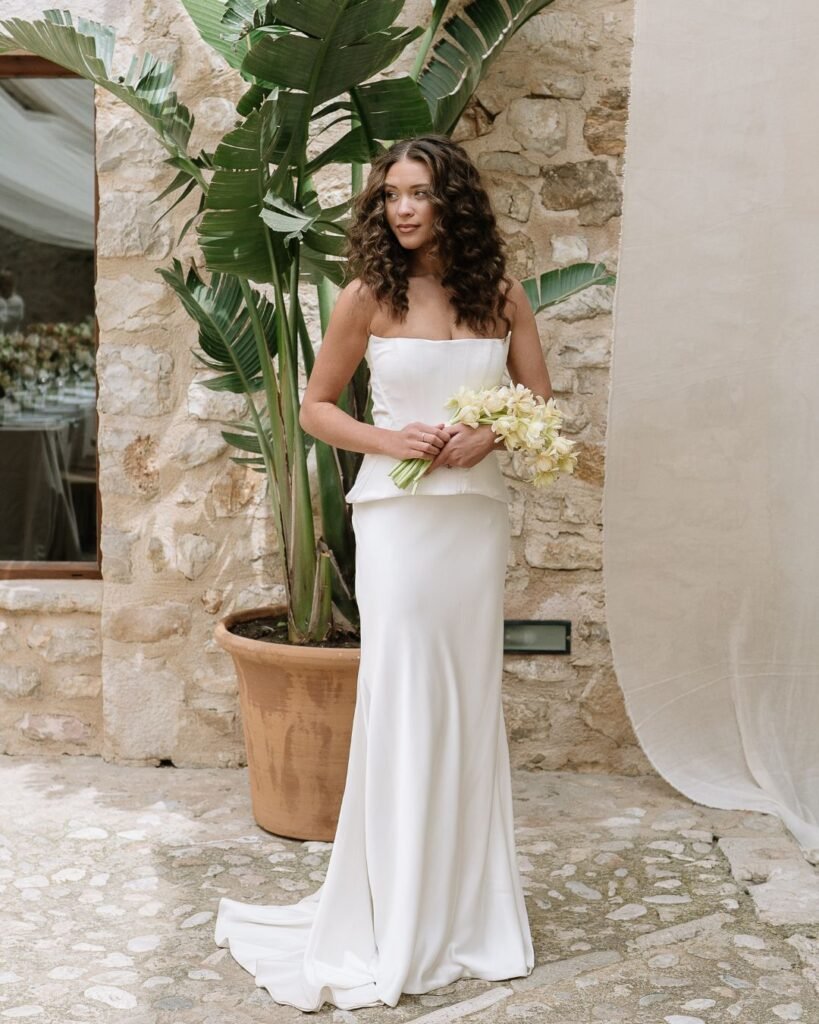 Bride posing gracefully with her elegant wedding dress and soft bouquet against a rustic stone backdrop at Finca Morneta.