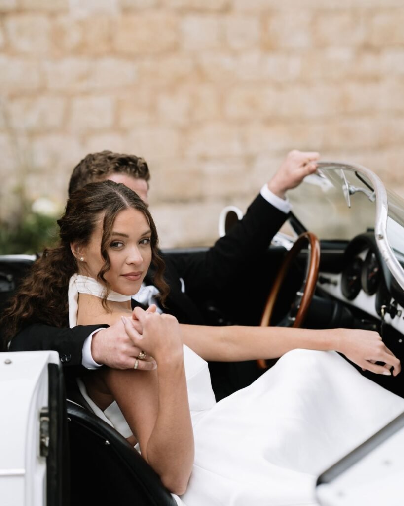 Bride and groom share an intimate moment seated in a classic car during their elegant wedding at Finca Morneta, captured by Sharon Cudworth