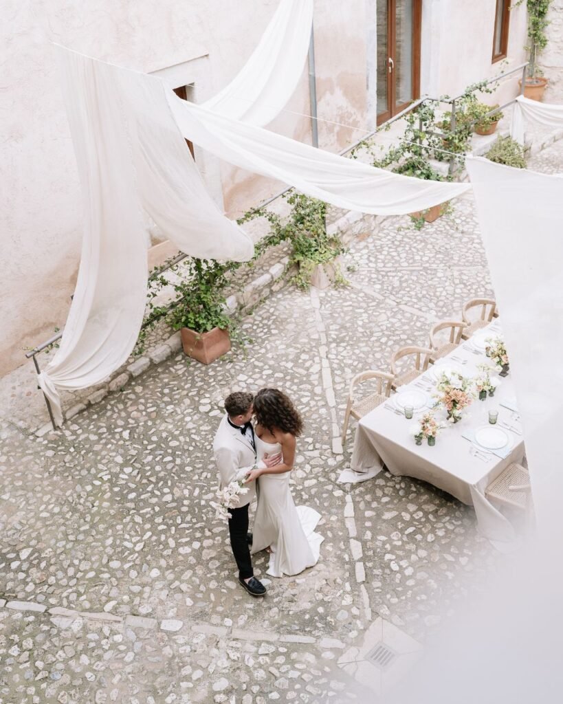 Romantic overhead perspective capturing newlyweds embracing in the idyllic courtyard of Finca Morneta, styled with delicate drapery and florals.