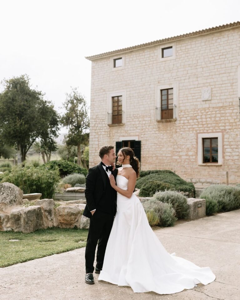 Bride and groom posing elegantly in front of Finca Morneta, highlighting the charming architecture and picturesque garden surroundings.