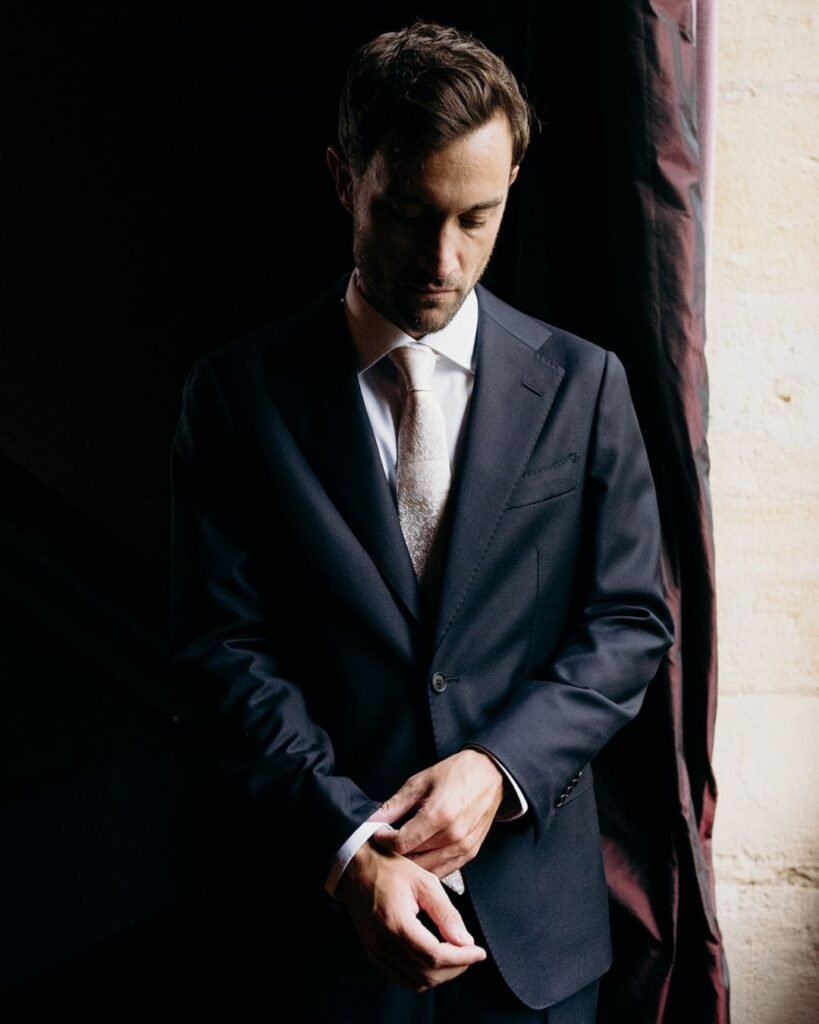 The groom adjusts his cufflinks by a window at Château Rigaud, captured in soft, moody light by Cleya Asulon.