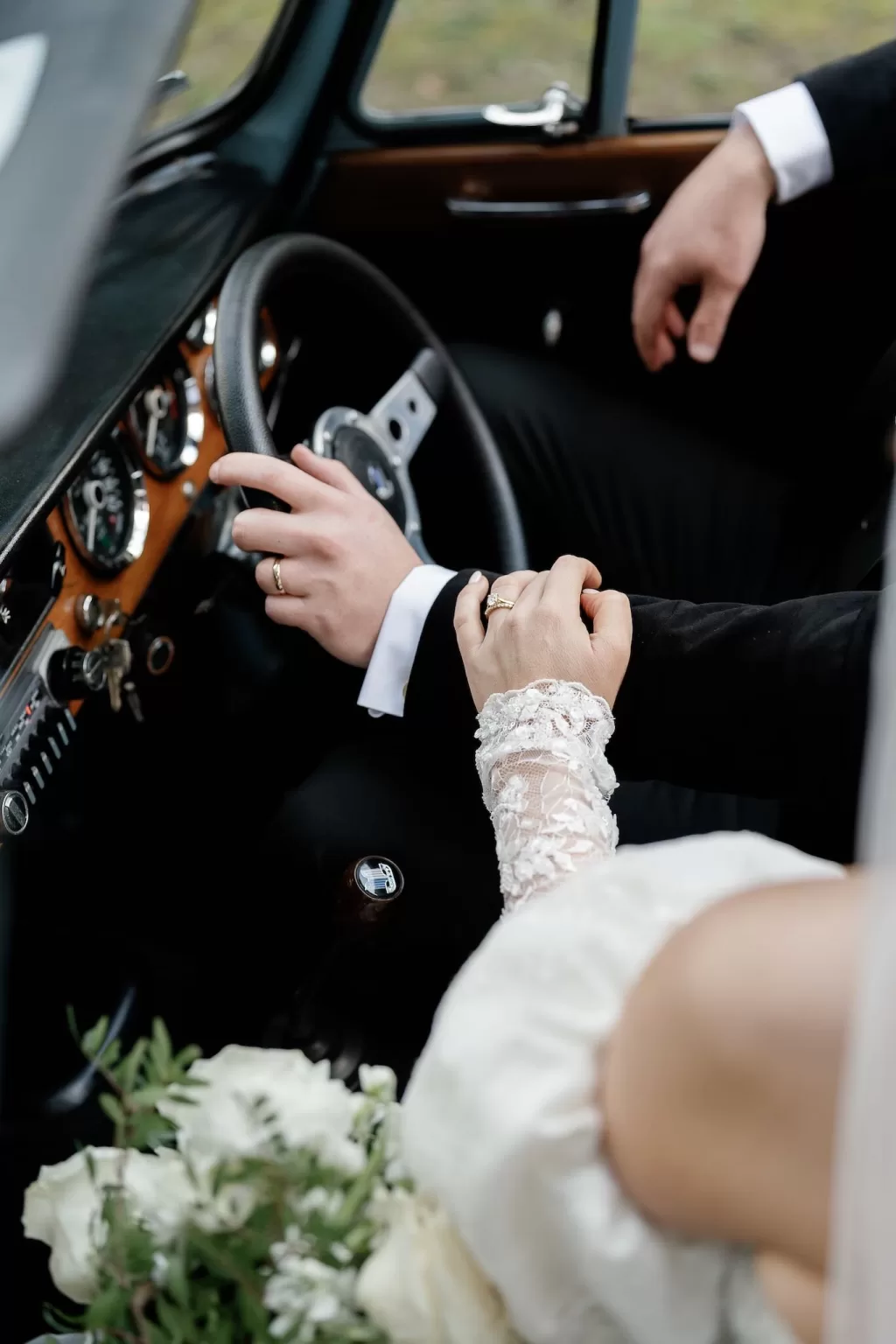 Intimate shot of bride and groom holding hands inside a vintage wedding car, captured by Sharon Cudworth.