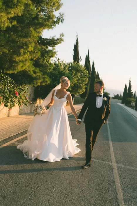 Newlyweds walk joyfully down a quiet Cyprus road outside Liopetro, lit by the soft glow of sunset.