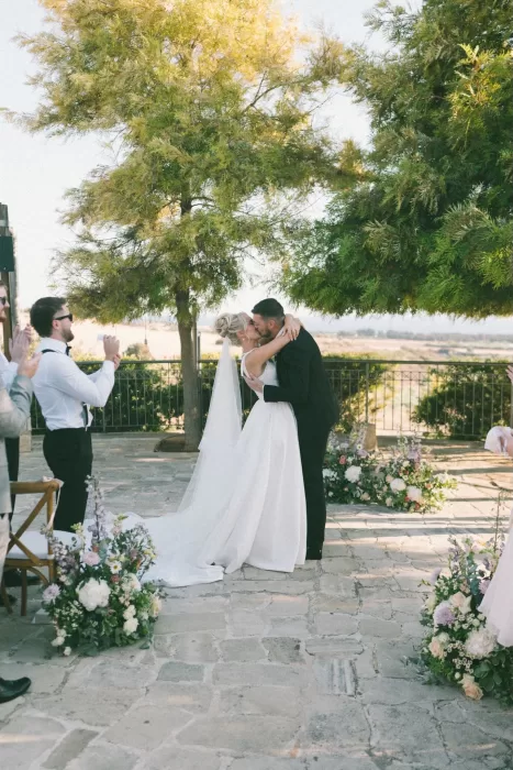 Just married couple share their first kiss under the Cyprus sun at Liopetro, surrounded by soft florals and cheers.
