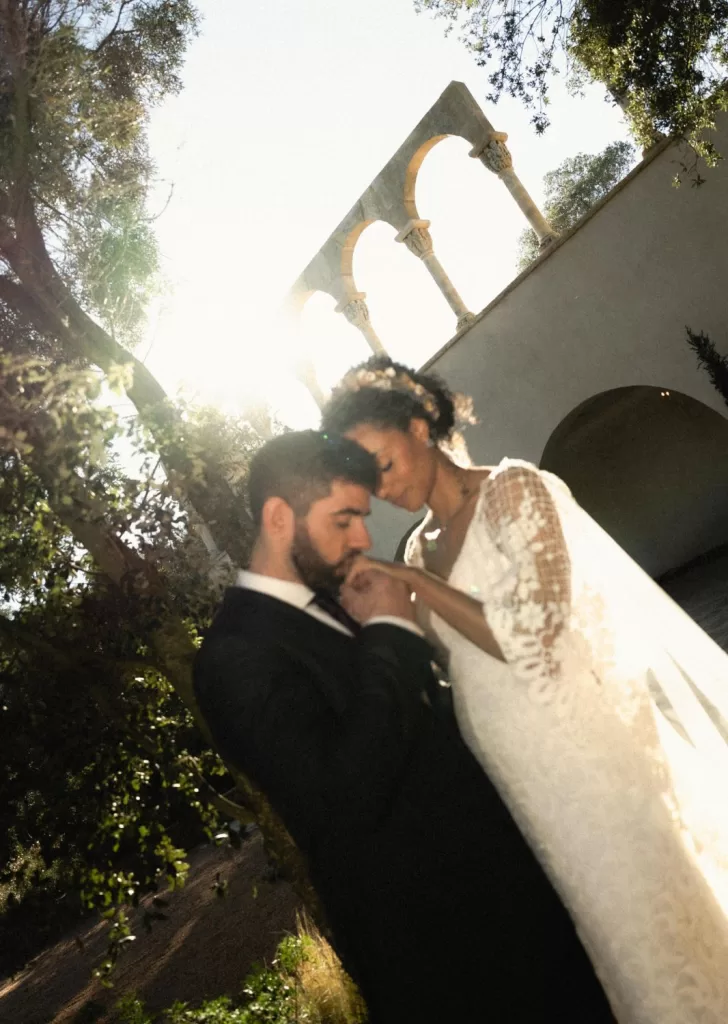 Tender moment between bride and groom beneath Mas Torroella’s sunlit arches.