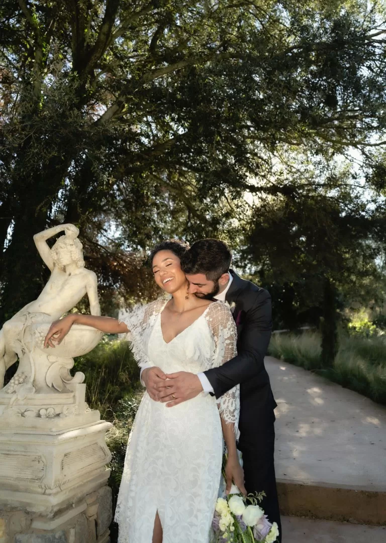 Joyful moment between bride and groom captured by a sculpture in Mas Torroella’s sunlit garden.