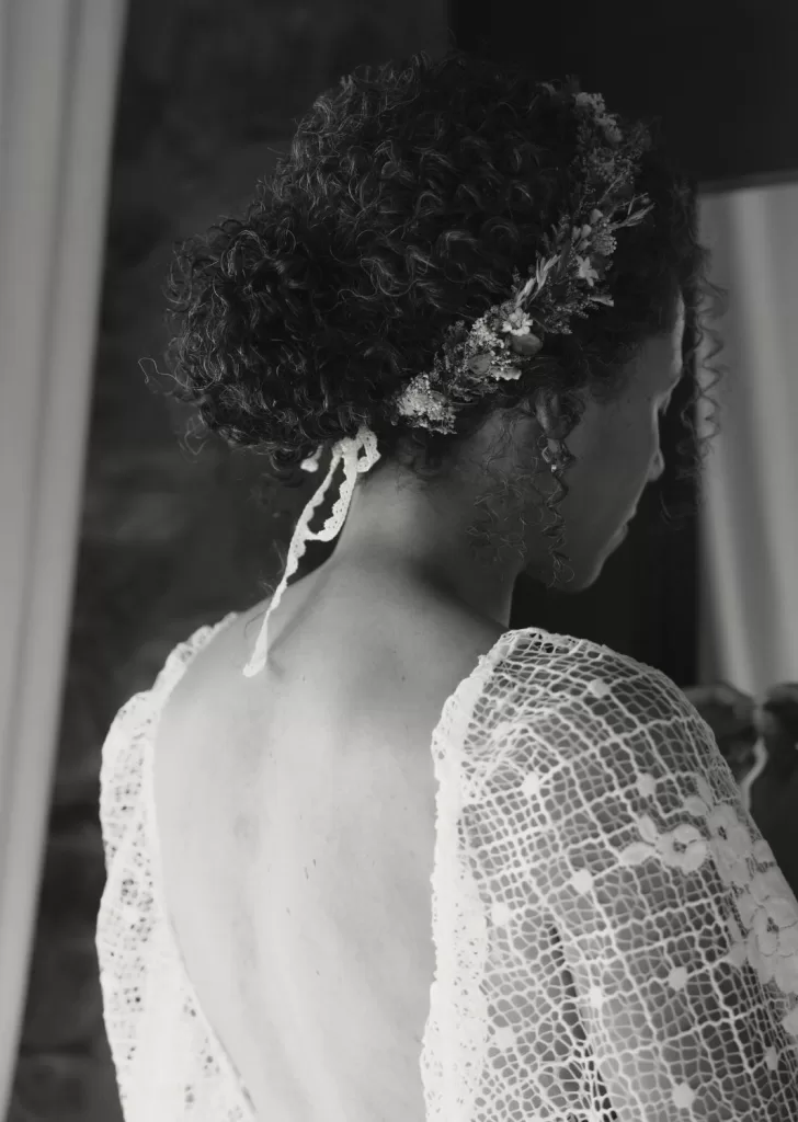 Bride with natural curls and a floral crown captured from behind, highlighting the lace dress and romantic styling at Mas Torroella.