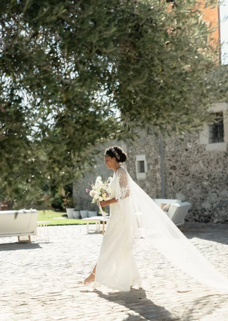 Bride walking gracefully across the cobbled courtyard at Mas Torroella with her bouquet and veil flowing behind.