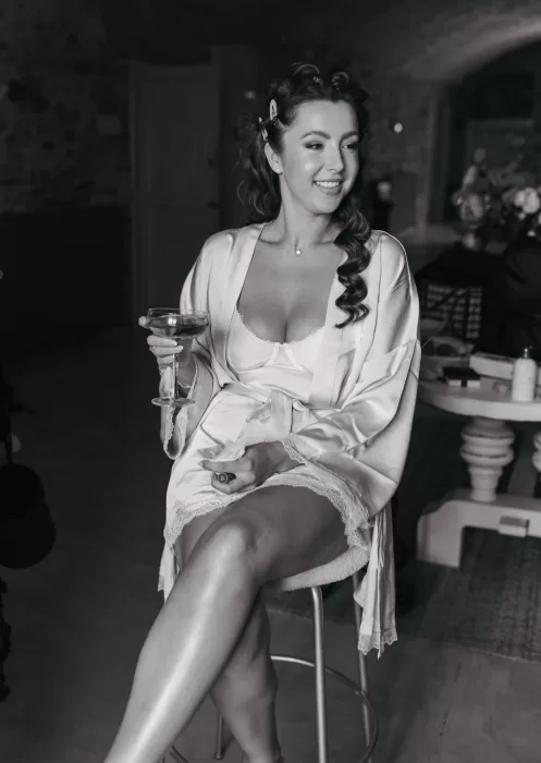 Bride in silk robe holding a glass of rosé, smiling during wedding morning at Mas Torroella.
