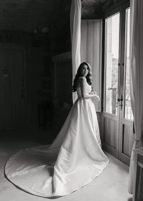 Bride standing in soft light by rustic window in bridal suite at Mas Torroella