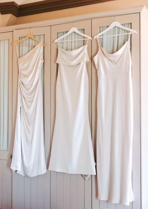 Three ivory satin bridesmaid dresses hanging neatly on a wardrobe at Mas Torroella.
