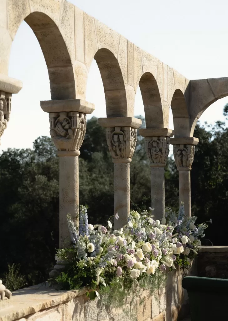 Romanesque stone arches adorned with soft pastel florals create a dreamy outdoor ceremony backdrop at Mas Torroella.