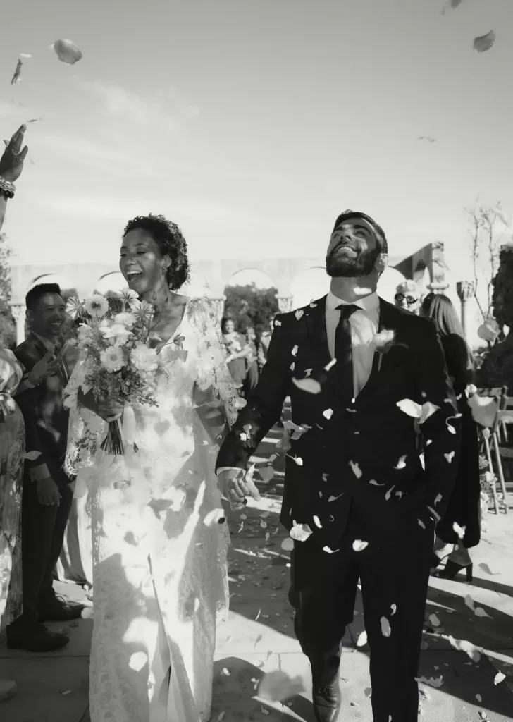 Just married couple laughing joyfully as flower petals fall during their confetti exit at Mas Torroella.