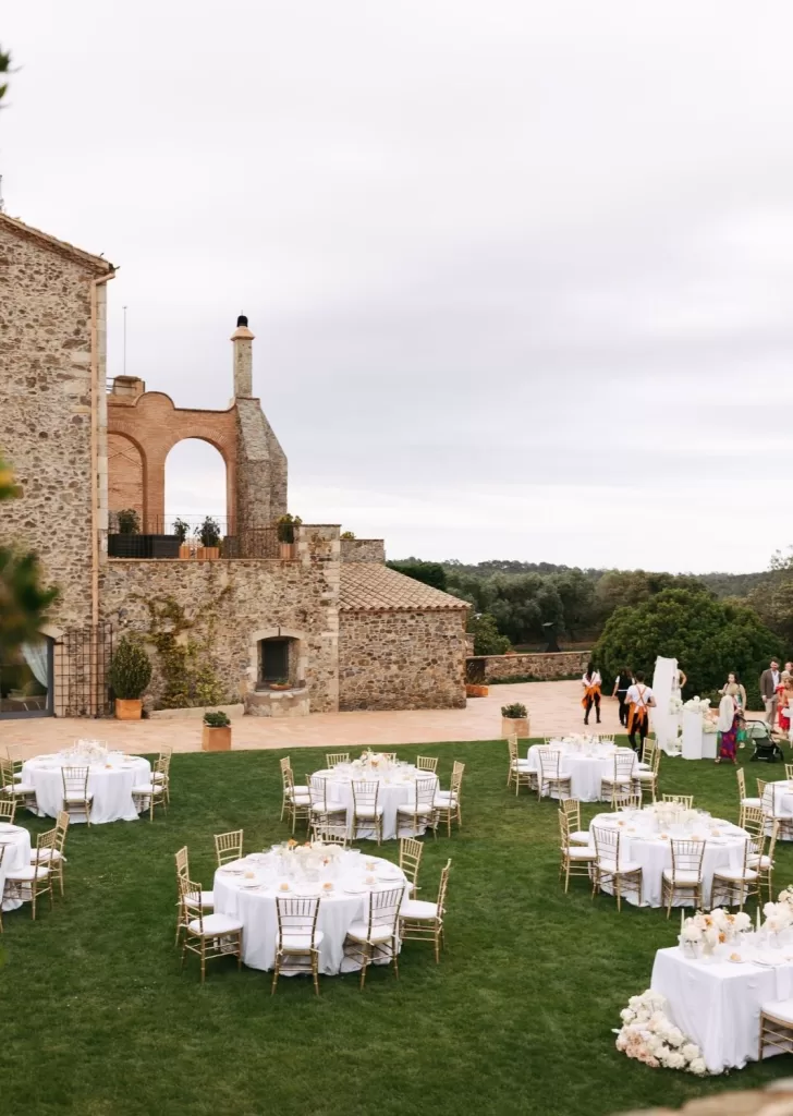 Outdoor wedding reception setup with round tables and gold chairs on the lawn at Mas Torroella.