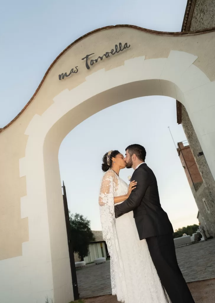 Bride and groom share a kiss under the arched entrance of Mas Torroella, just after their ceremony.