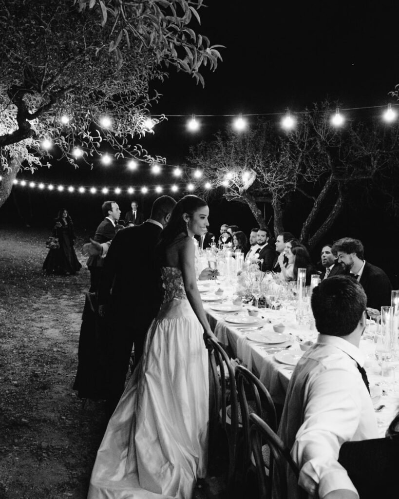 Bride in elegant gown standing at candlelit outdoor dinner under string lights at Masia Cabellut.
