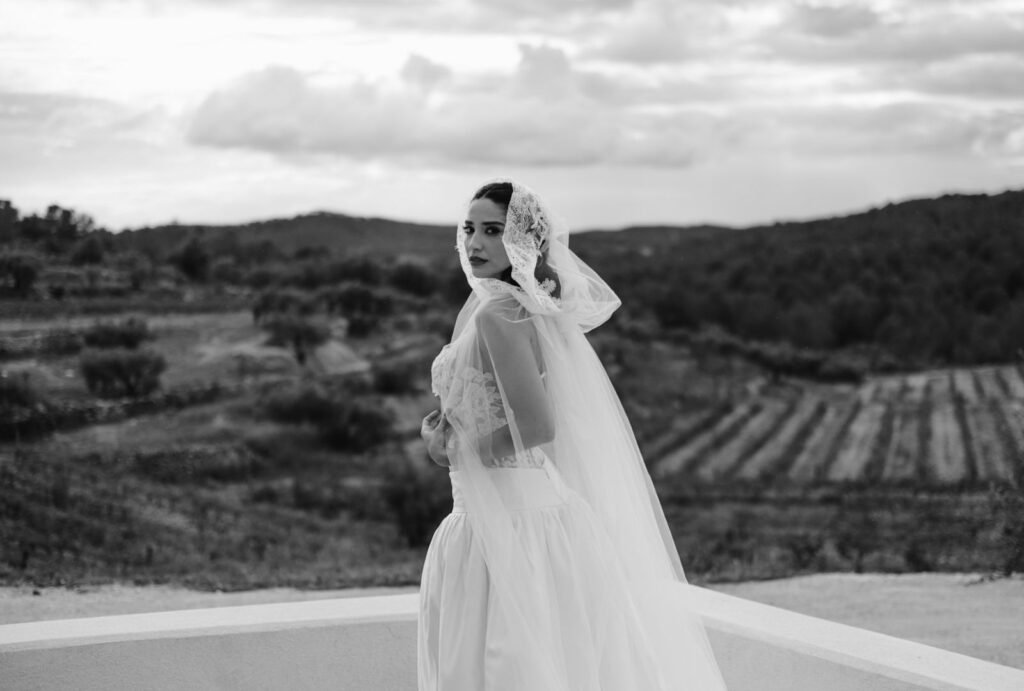 Black-and-white portrait of a bride wearing a delicate veil and gown, standing against the serene countryside backdrop at Masia Cabellut.