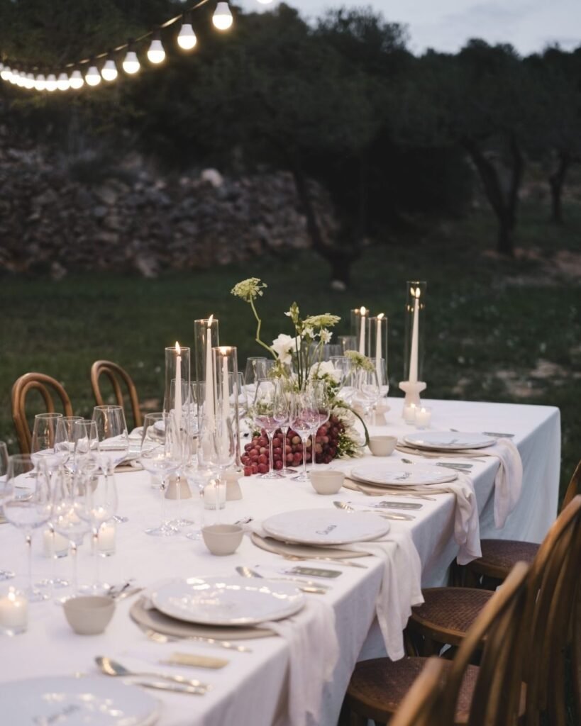 Candlelit wedding table at Masia Cabellut with white linens, florals and grapes beneath glowing string lights.