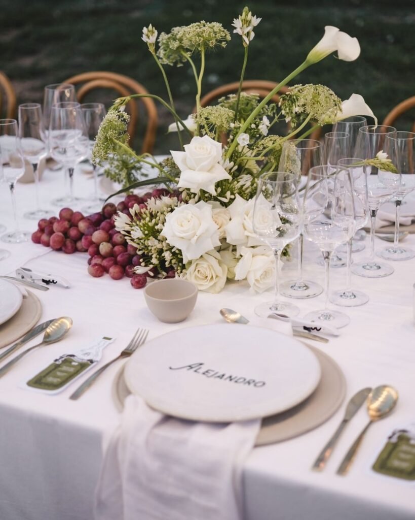 Place setting for Alejandro with white roses and grapes at Masia Cabellut wedding.