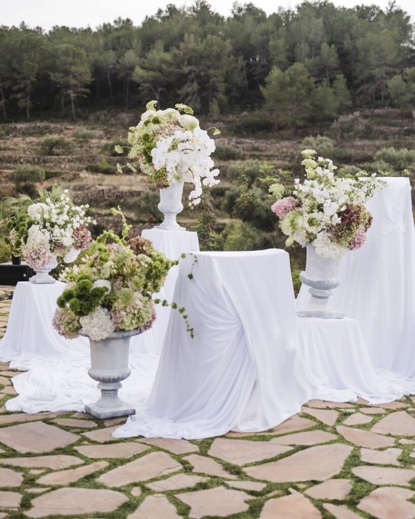 Elegant white-draped pedestals adorned with lush floral arrangements for an outdoor ceremony at Masia Cabellut.