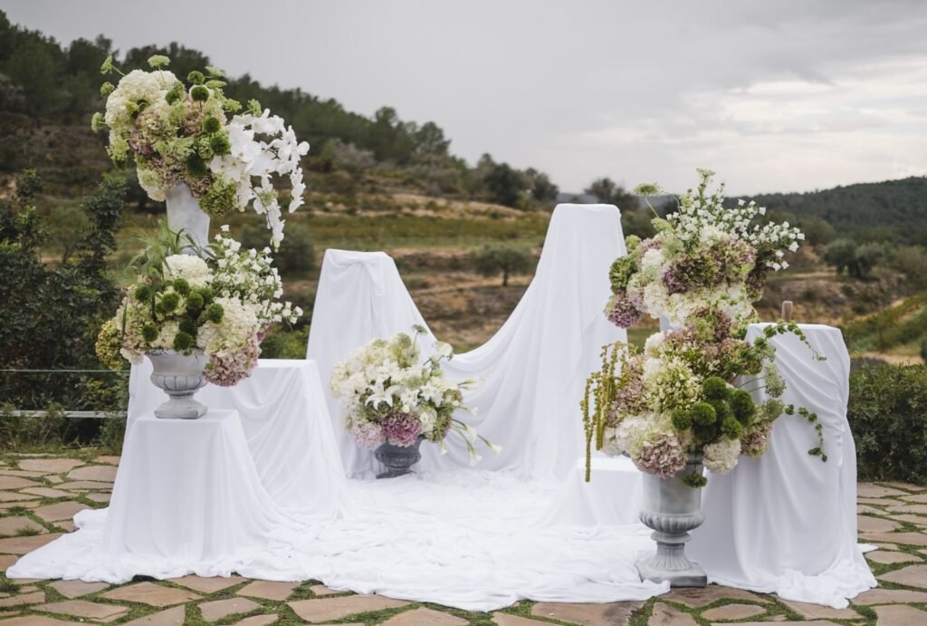 Beautifully styled wedding altar decorated with lush white and pastel floral arrangements set against the scenic landscape of Masia Cabellut.