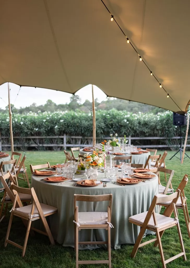 Wedding table decor with a centerpiece of white and orange flowers, a card reading "Prawn Linguine," and delicate glassware