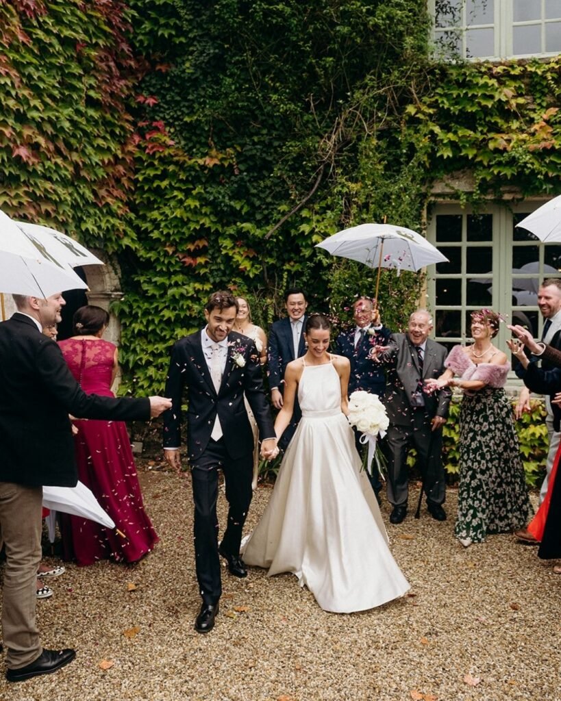 Bride and groom walk through confetti and umbrellas after their Château Rigaud ceremony, surrounded by cheering guests.