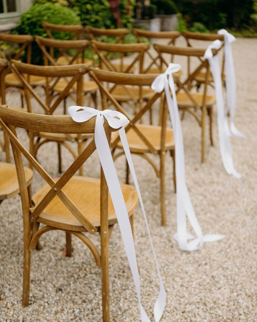 Close-up of wooden chairs with long white ribbons lining the aisle for an outdoor wedding ceremony at Château Rigaud.