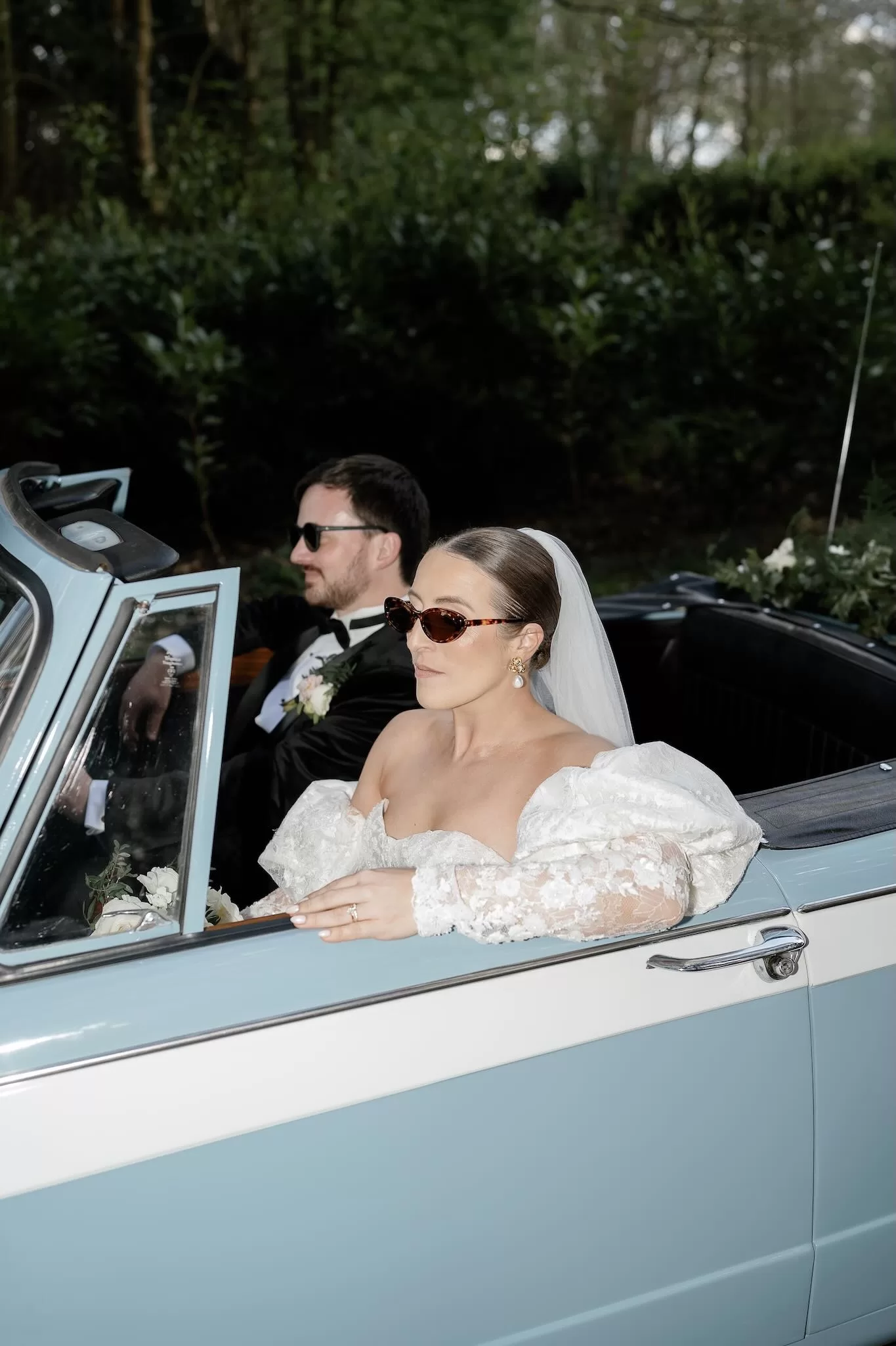 Bride and groom stylishly driving away in powder blue vintage convertible, photographed by Sharon Cudworth.