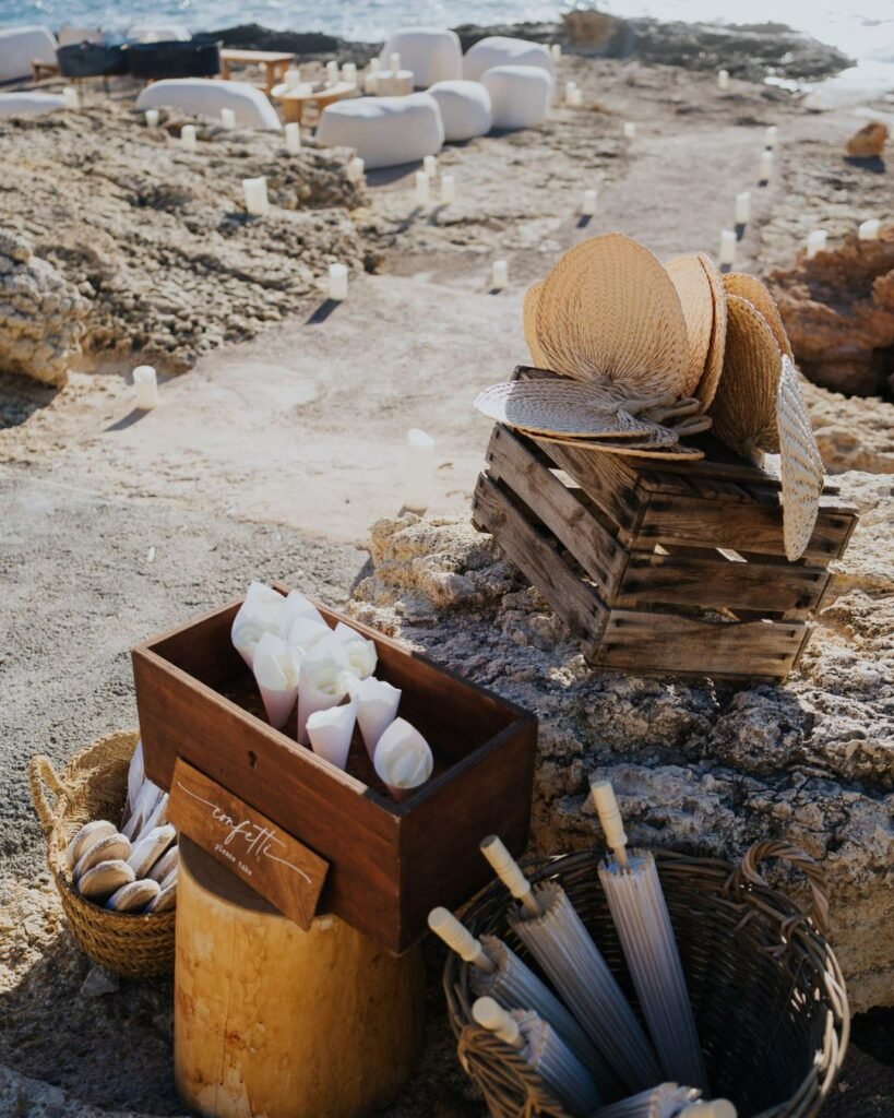Ceremony setup at Six Senses Ibiza with parasols, fans, and rose petal confetti on rustic coastal rocks.