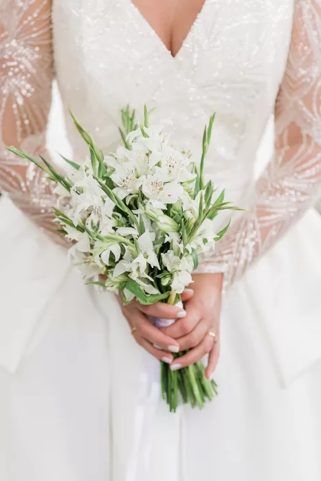 Close-up of bride’s white lily bouquet against her beaded wedding gown at Uzutrakio Dvaras.