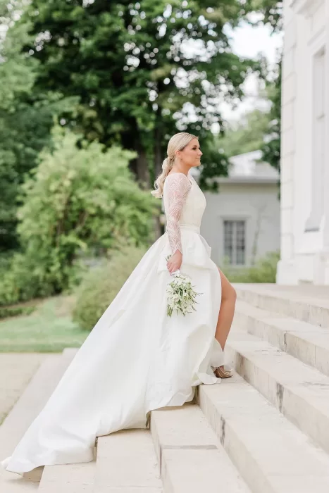 Bride in elegant gown holding bouquet while walking up stone steps at Uzutrakio Dvaras.