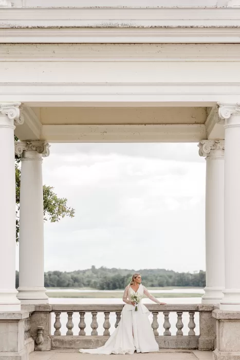 Bride standing under classical white stone arch at Uzutrakio Dvaras.
