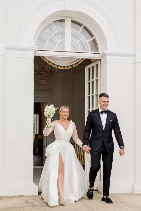 Bride and groom make a joyful grand entrance through the elegant doors of Uzutrakio Dvaras.