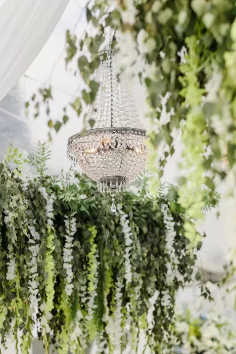 Crystal chandelier surrounded by greenery at Uzutrakio Dvaras wedding reception.