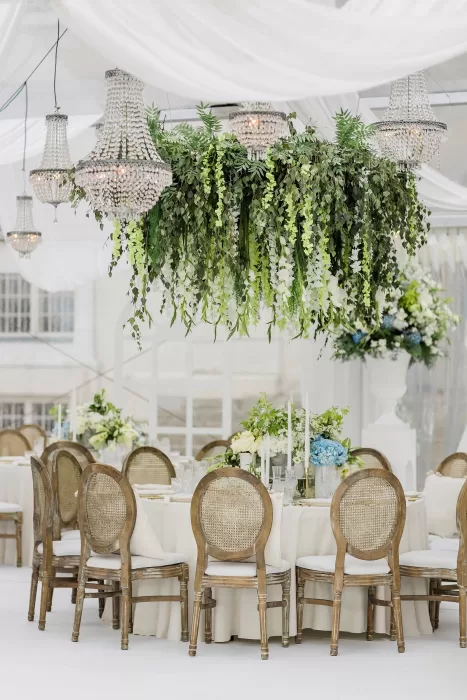 Wedding reception tables decorated with lush greenery and crystal chandeliers at Uzutrakio Dvaras.