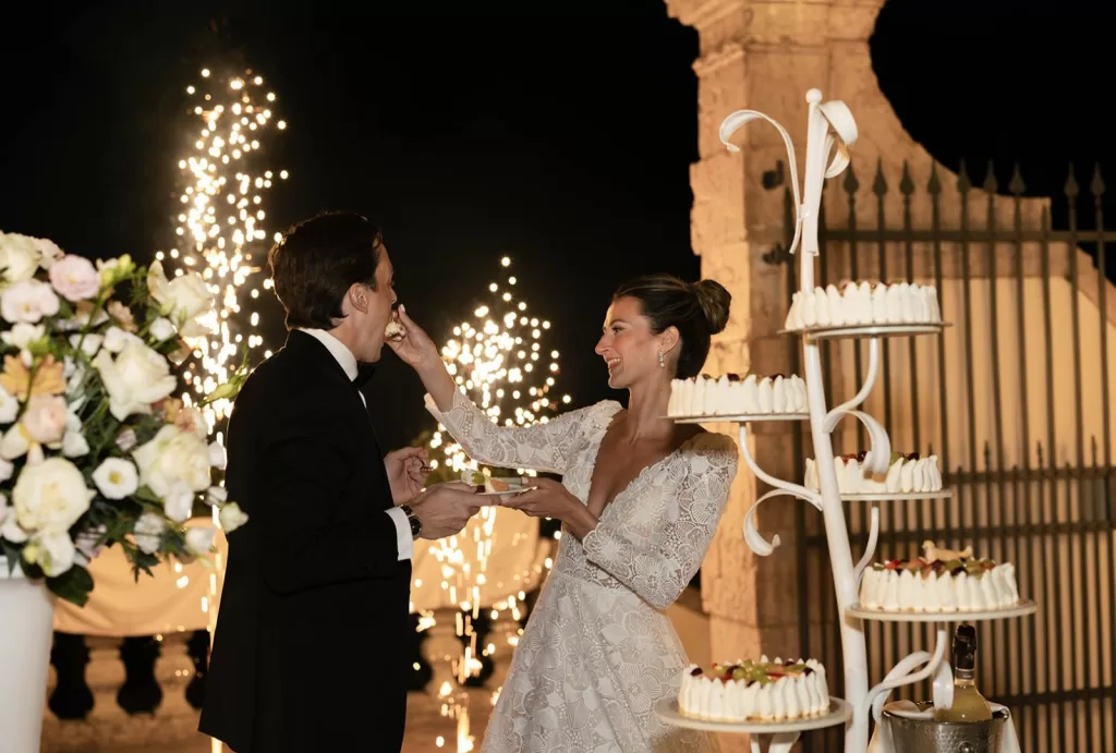 Bride feeds the groom a slice of wedding cake with sparklers glowing behind them at Villa Cariola.