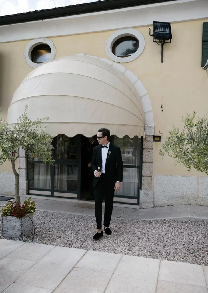 Groom stepping outside the entrance of Villa Cariolla, drink in hand, ready for the celebration to begin.