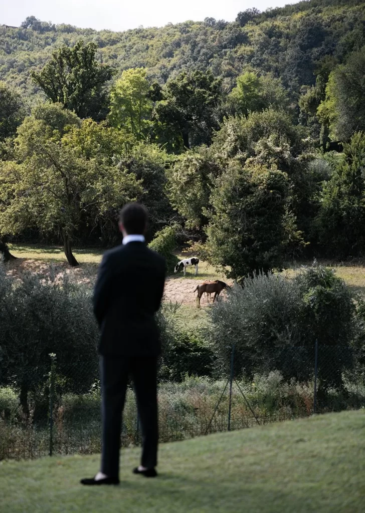 Groom gazing at grazing horses in the distance, framed by lush countryside at Villa Cariolla.