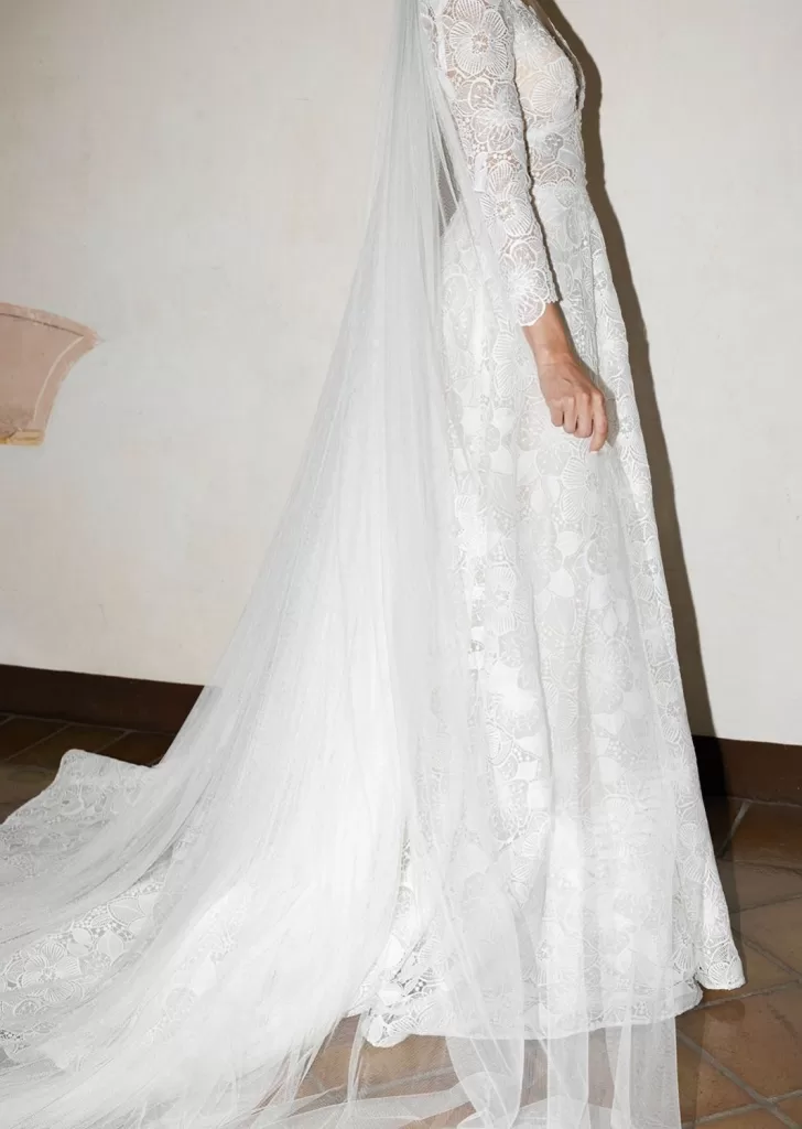 Side view of the bride’s floral lace gown with a flowing veil against Villa Cariolla’s neutral interior wall.