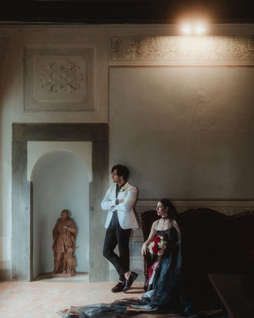 Bride and groom captured in moody window light at Villa Ivana, standing near a terracotta statue and vintage furniture.