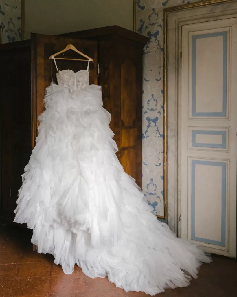 The wedding dress hangs elegantly in a sunlit room, awaiting the bride’s final touches.