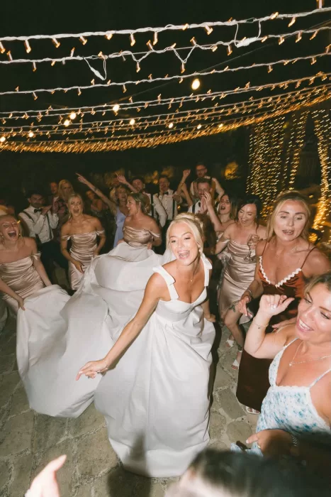 Bride leads a lively dance floor moment surrounded by bridesmaids and guests under glowing string lights at Liopetro.