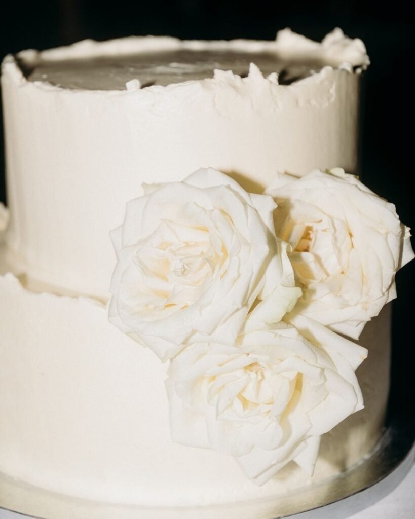 Minimalist two-tier white wedding cake adorned with fresh white roses at Château Rigaud.