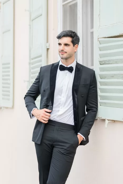 Groom adjusting his tailored blazer on a stone terrace overlooking Bastide du Roy’s manicured gardens, exuding confidence and refined style.