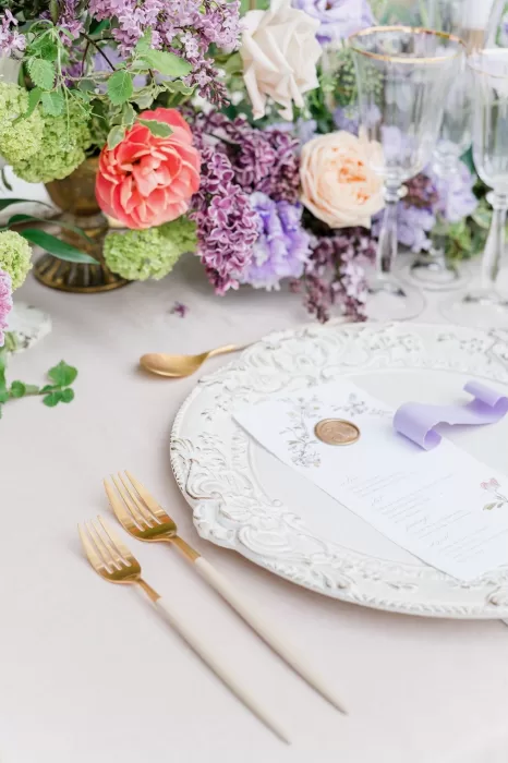 Close-up of an elegant place setting at Bastide du Roy, featuring gold-rimmed glassware, fine china, and delicate floral napkin rings on crisp linens.