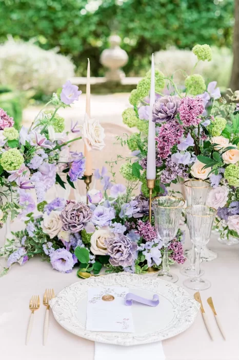 Long heirloom dining table set for a wedding at Bastide du Roy, illuminated by candlelit lanterns and decorated with verdant centerpieces on crisp white linens.