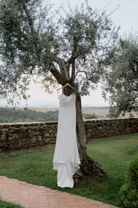 Bridal gown hanging from an olive tree with Tuscan hills in the background at Borgo Sant Ambrogio.