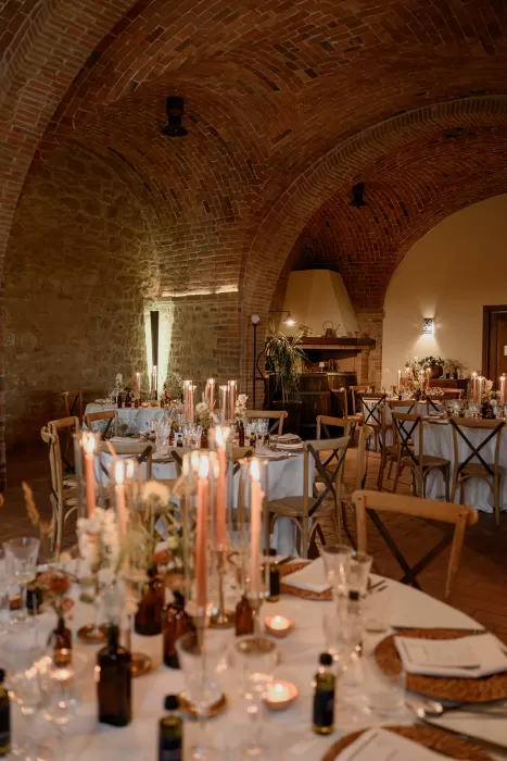 Elegant wedding reception setup at Borgo Sant Ambrogio, with candlelit tables under vaulted brick ceilings and soft ambient lighting.